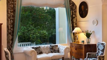 A room with a white sofa, a wooden cabinet, a chair, a table, and a window with curtains.
