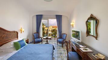 A hotel room with a bed, two chairs, a desk with a computer, and a TV.