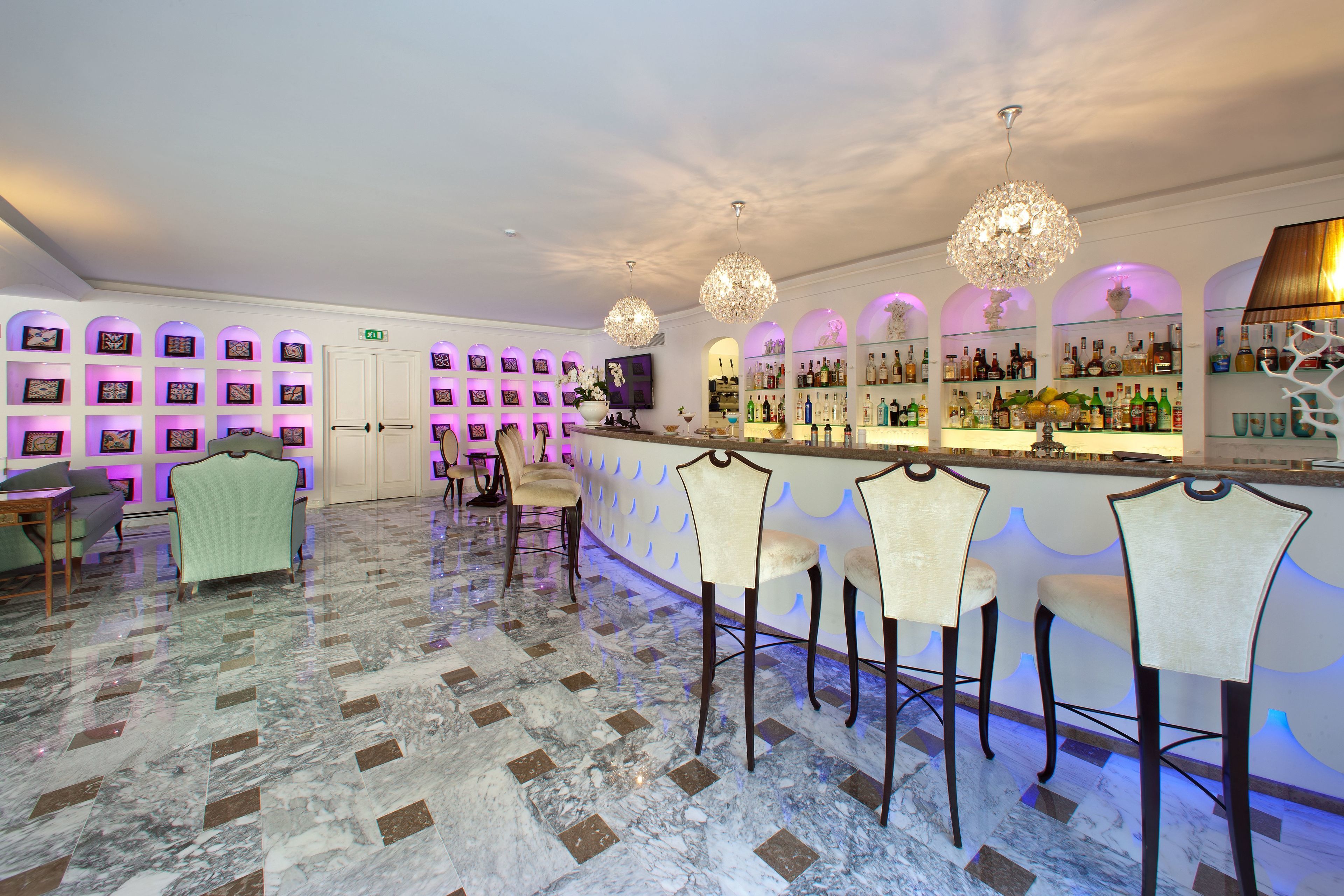 A bar area with marble flooring, bar stools, and a wall of framed pictures.