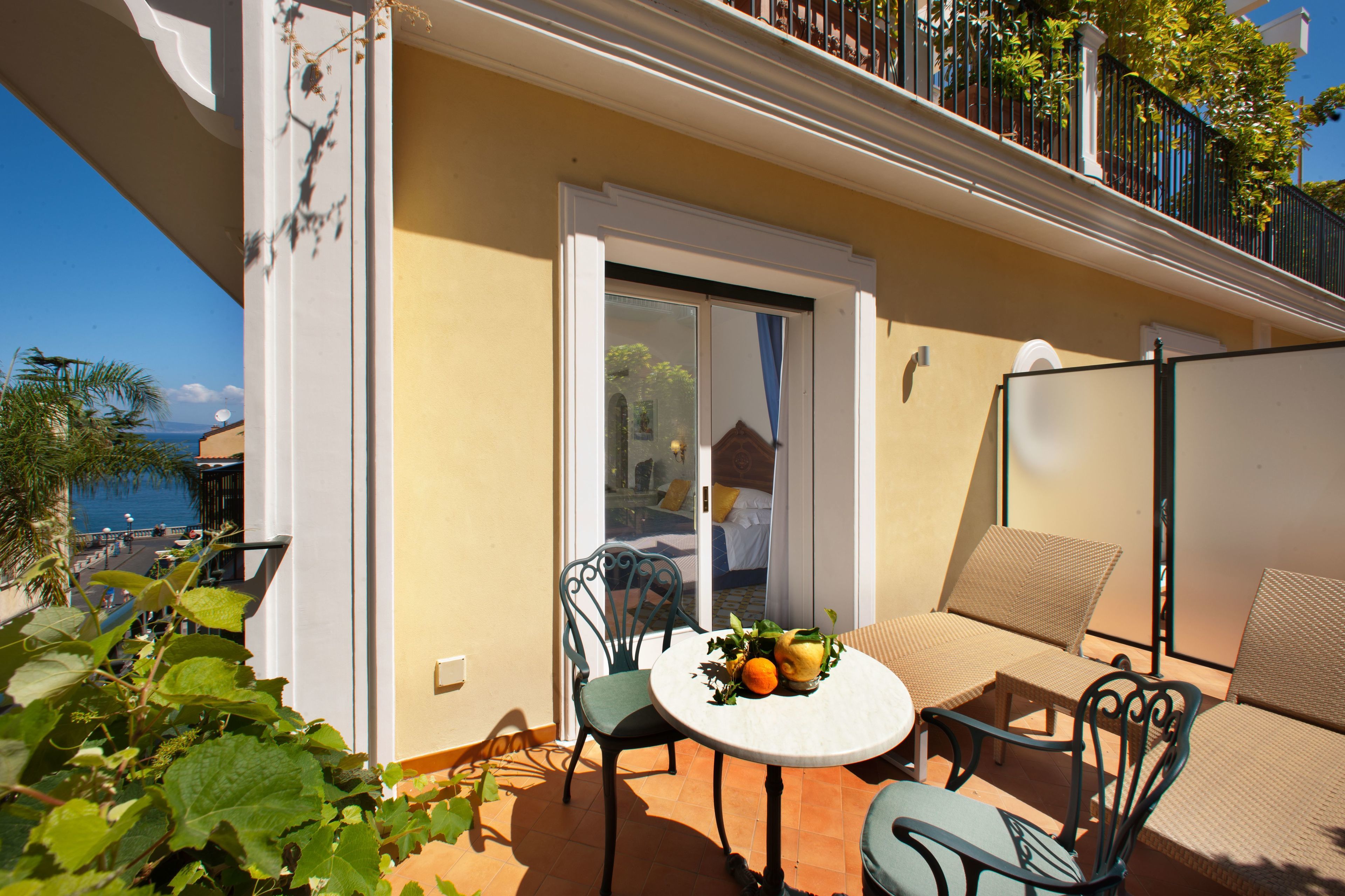 A balcony with a table and chairs, a small table with fruit, and a view of the sea.