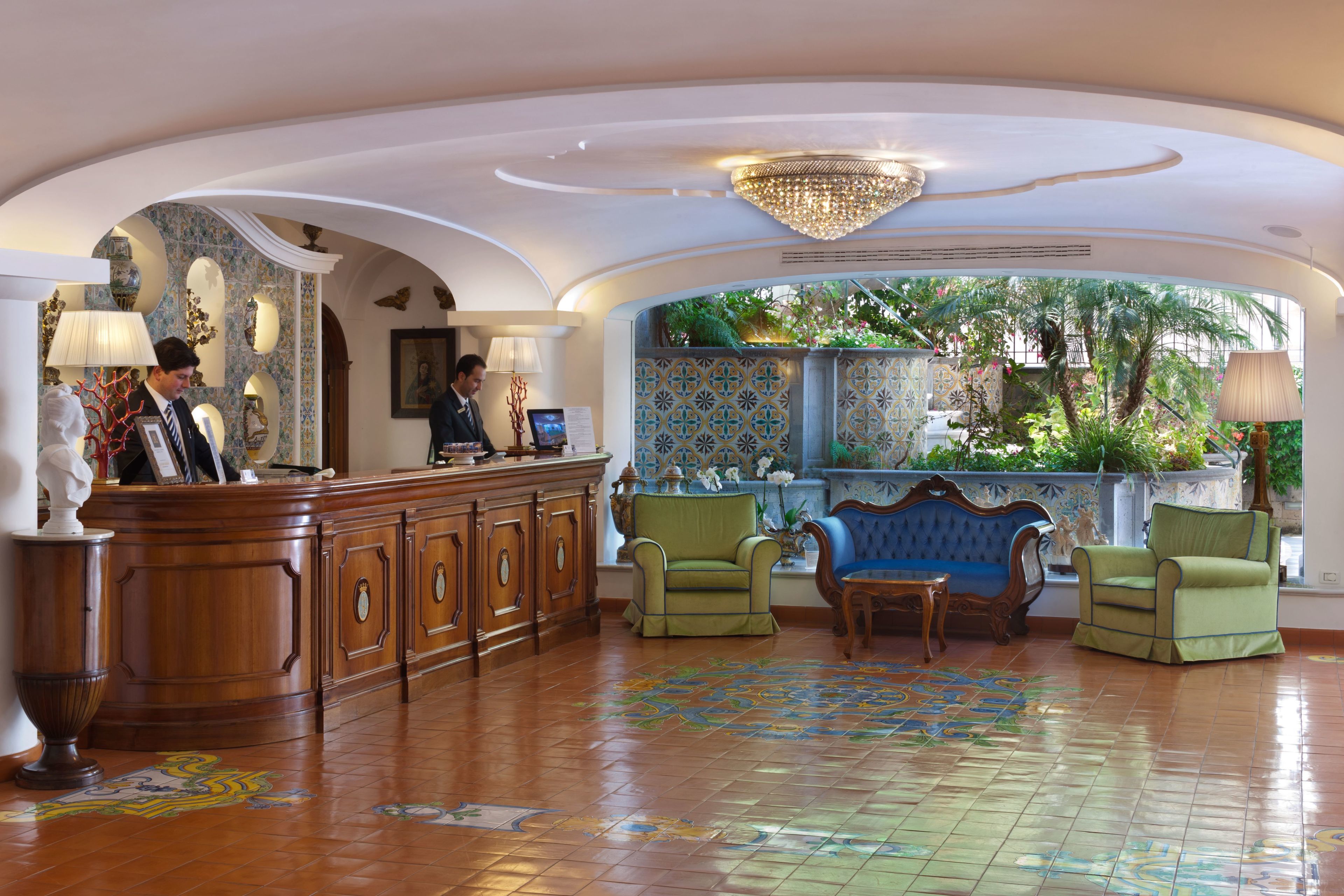 A lobby with a reception desk, two green armchairs, a blue sofa, and a patterned floor.