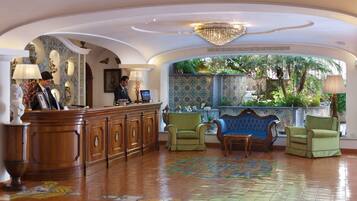 A lobby with a reception desk, two green armchairs, a blue sofa, and a patterned floor.