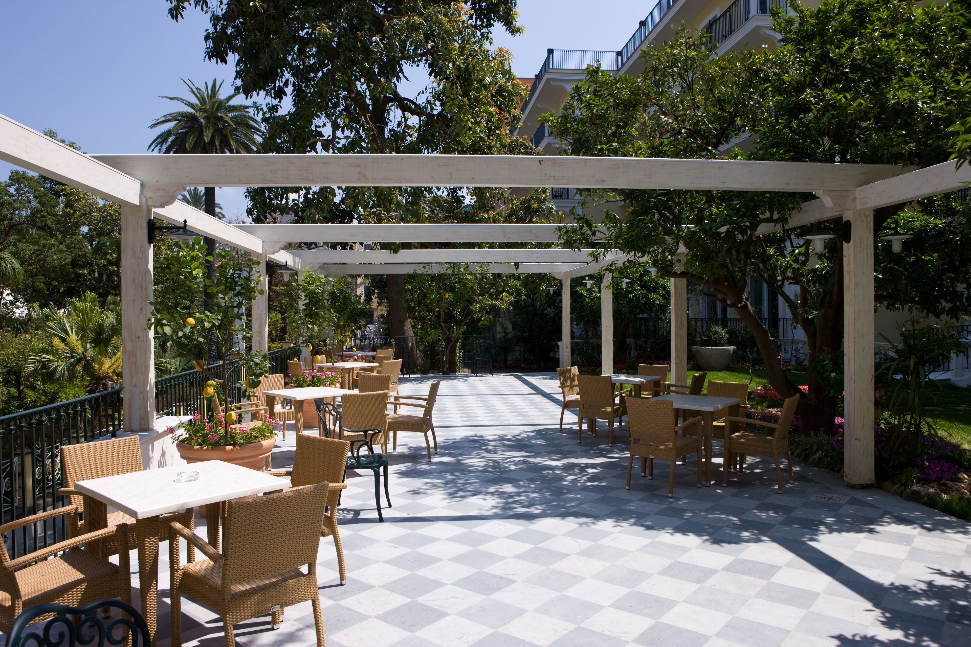 An outdoor patio with checkered flooring, wicker furniture, and a pergola structure.