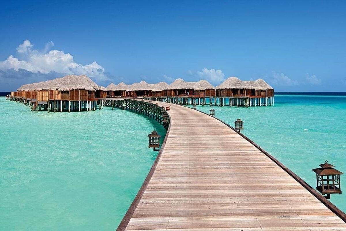 A wooden pier leading to overwater bungalows with thatched roofs.