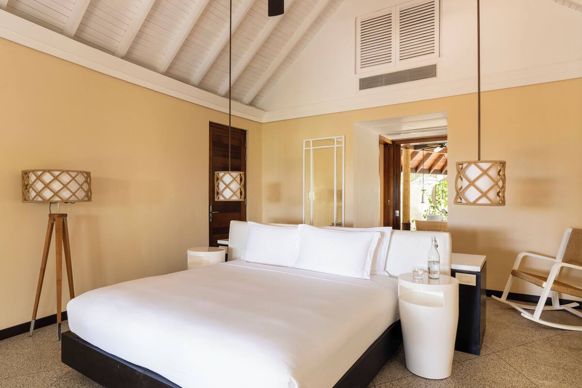 A spacious bedroom with a large bed, bedside tables, a chair, and a hanging lamp.