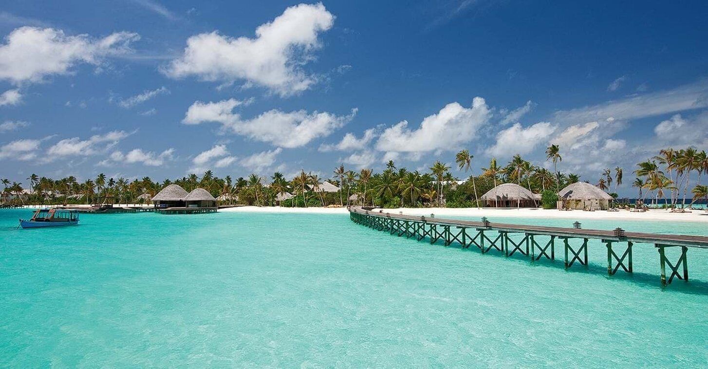A tropical beach resort with overwater bungalows, a wooden pier, and clear turquoise waters.