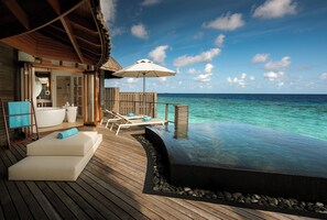 An infinity pool with a wooden deck, lounge chairs, and a thatched roof structure. - Constance Halaveli (Halaveli)