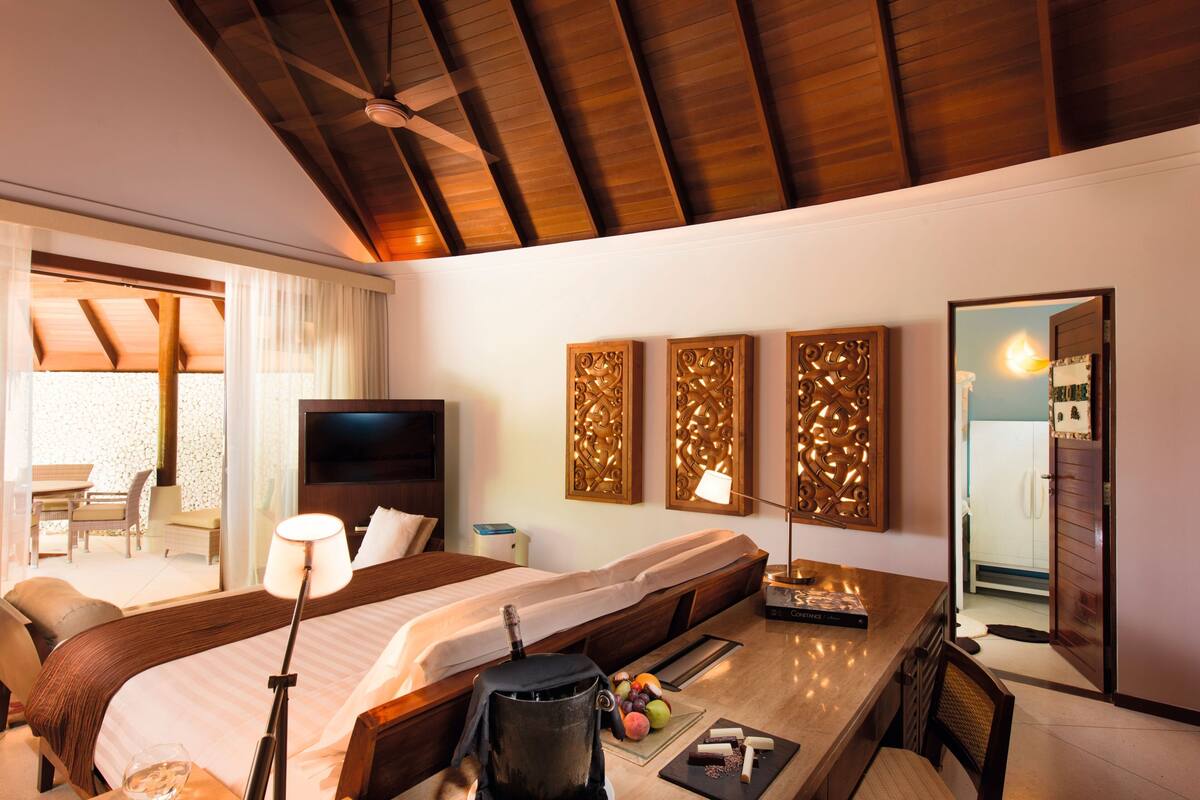A hotel room with a large bed, a desk, a chair, a TV, and a balcony with a table and chairs.