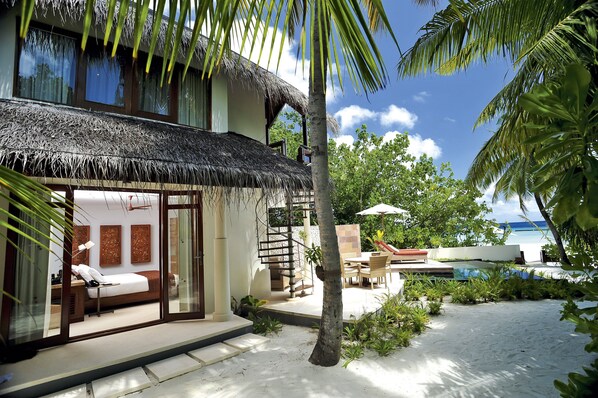 A beachfront villa with a thatched roof, a private pool, and a bedroom with a large bed and a desk. - Constance Halaveli (Halaveli)