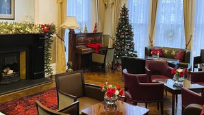 Un vaste salon agrémenté d’un magnifique lustre, d’un piano, d’un sapin de Noël et de coins salon confortables.