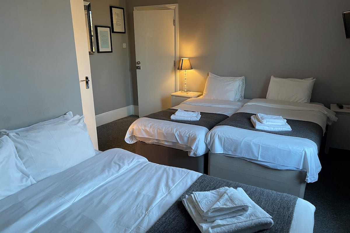 A hotel room with two single beds, a double bed, a bedside table with a lamp, and a door.