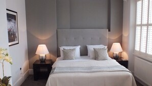 Une chambre à coucher avec un grand lit, deux tables de chevet avec des lampes, une plante en pot et une fenêtre avec des stores.