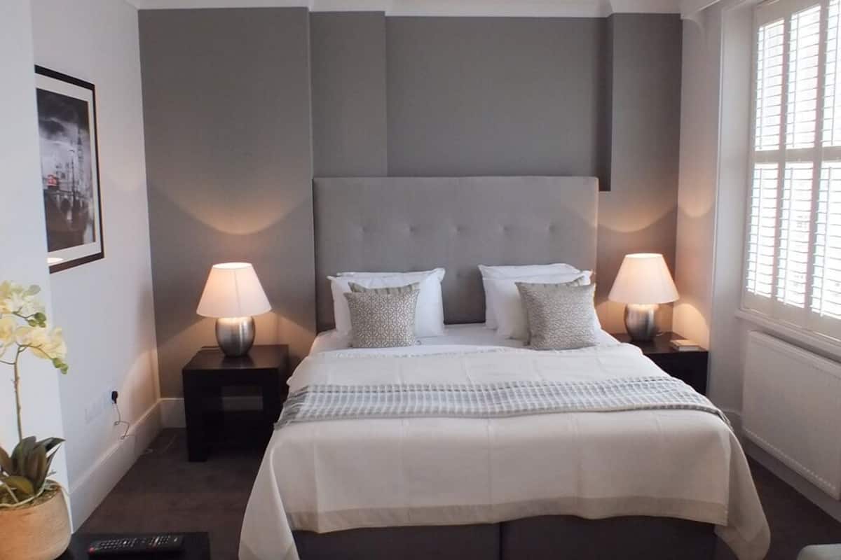 A bedroom with a large bed, two bedside tables with lamps, a potted plant, and a window with blinds.