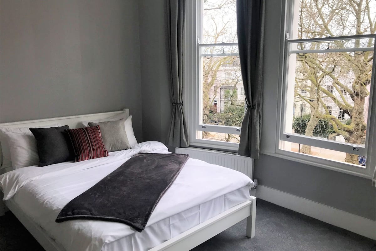 A bedroom with a bed, white headboard, grey walls, and a window with curtains.