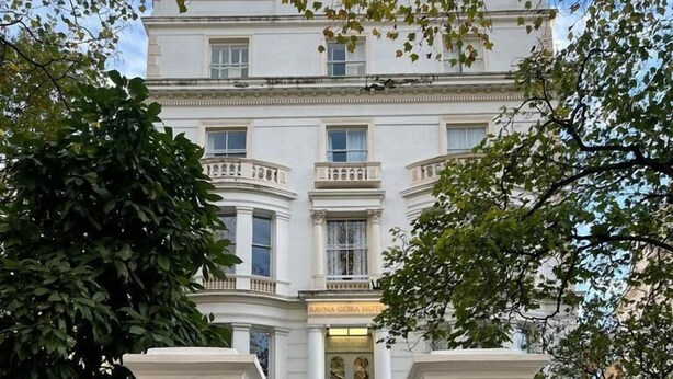 Un bâtiment blanc avec une enseigne indiquant « HÔTEL RAYNA GORA » à l’entrée.