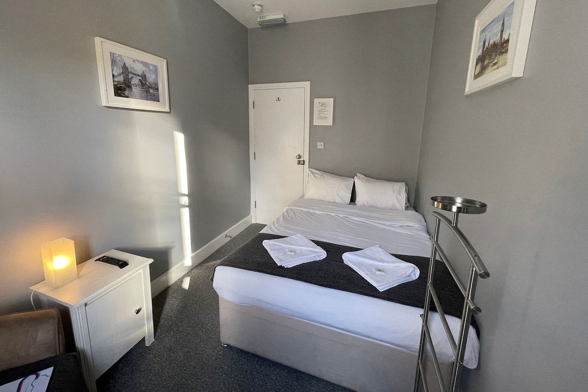 A hotel room with a bed, bedside table, lamp, and a picture on the wall.