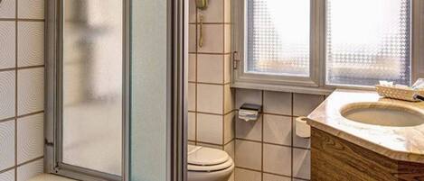 A bathroom with a bathtub, toilet, and a window with frosted glass.