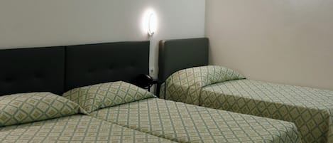 A hotel room with two beds, a headboard, a wall-mounted light fixture, and a geometric wall decoration.