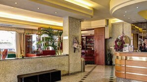A hotel lobby with a reception desk, a seating area, and a large plant.