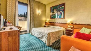 A hotel room with a bed, a desk with a lamp, a chair, a sofa, and a painting on the wall.