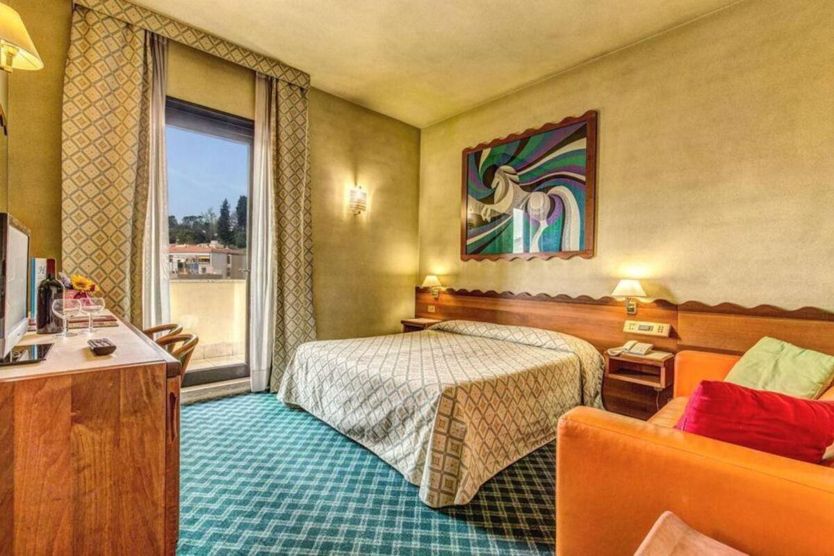 Ein Hotelzimmer mit einem Bett, einem Schreibtisch mit Lampe, einem Sessel und einem Sofa, sowie einem Bild an der Wand.