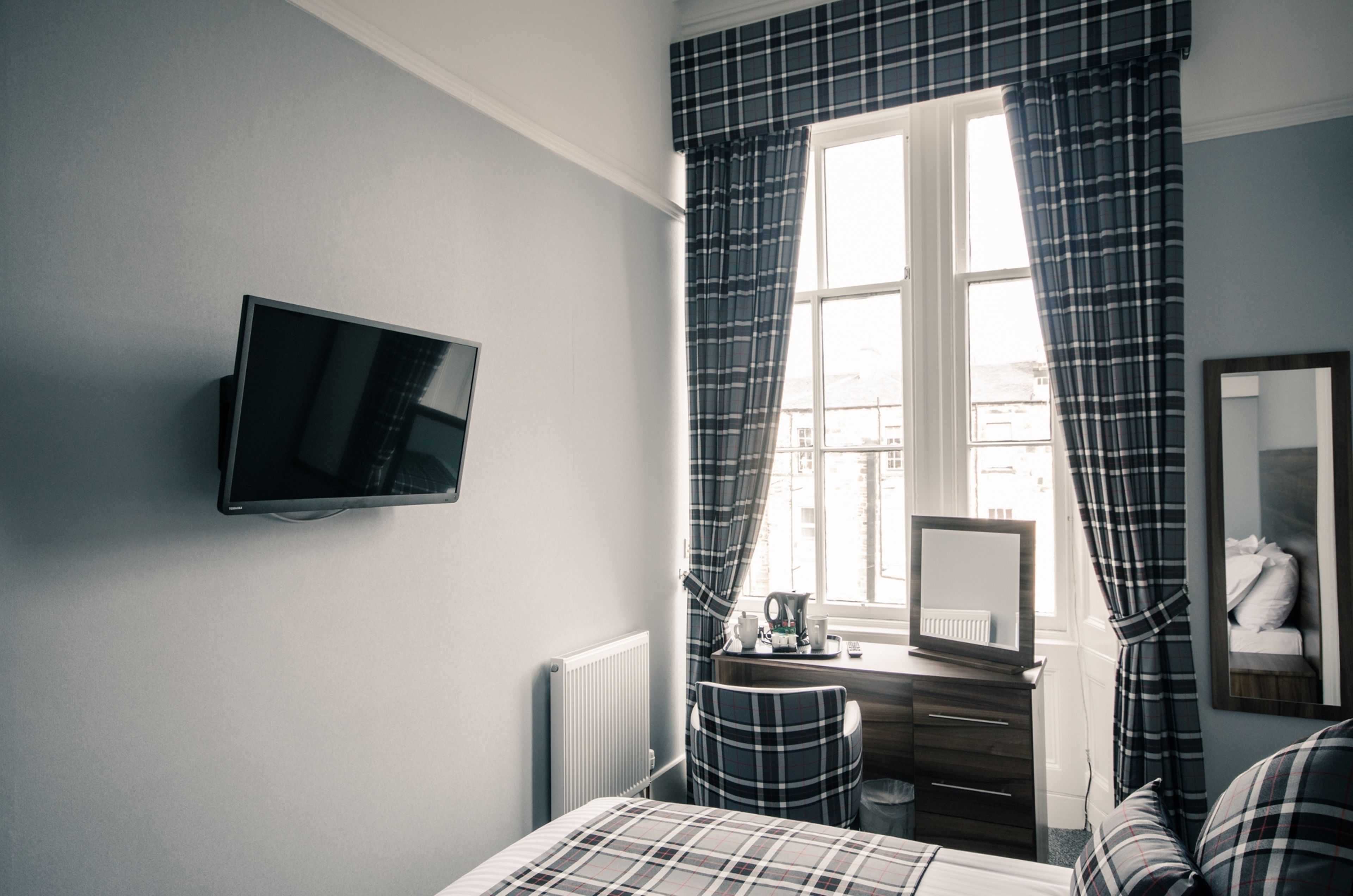 A bedroom with a bed, a TV, a dresser, a mirror, and a window with curtains.