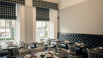 Un restaurante con una decoración clásica, que presenta un sillón de cuero negro, sillas de madera blanca y mesas dispuestas para comer.