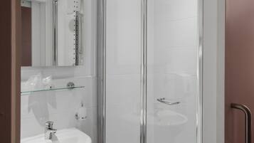 Un baño moderno con ducha de vidrio, lavamanos pedestal y espejo sobre el lavamanos.