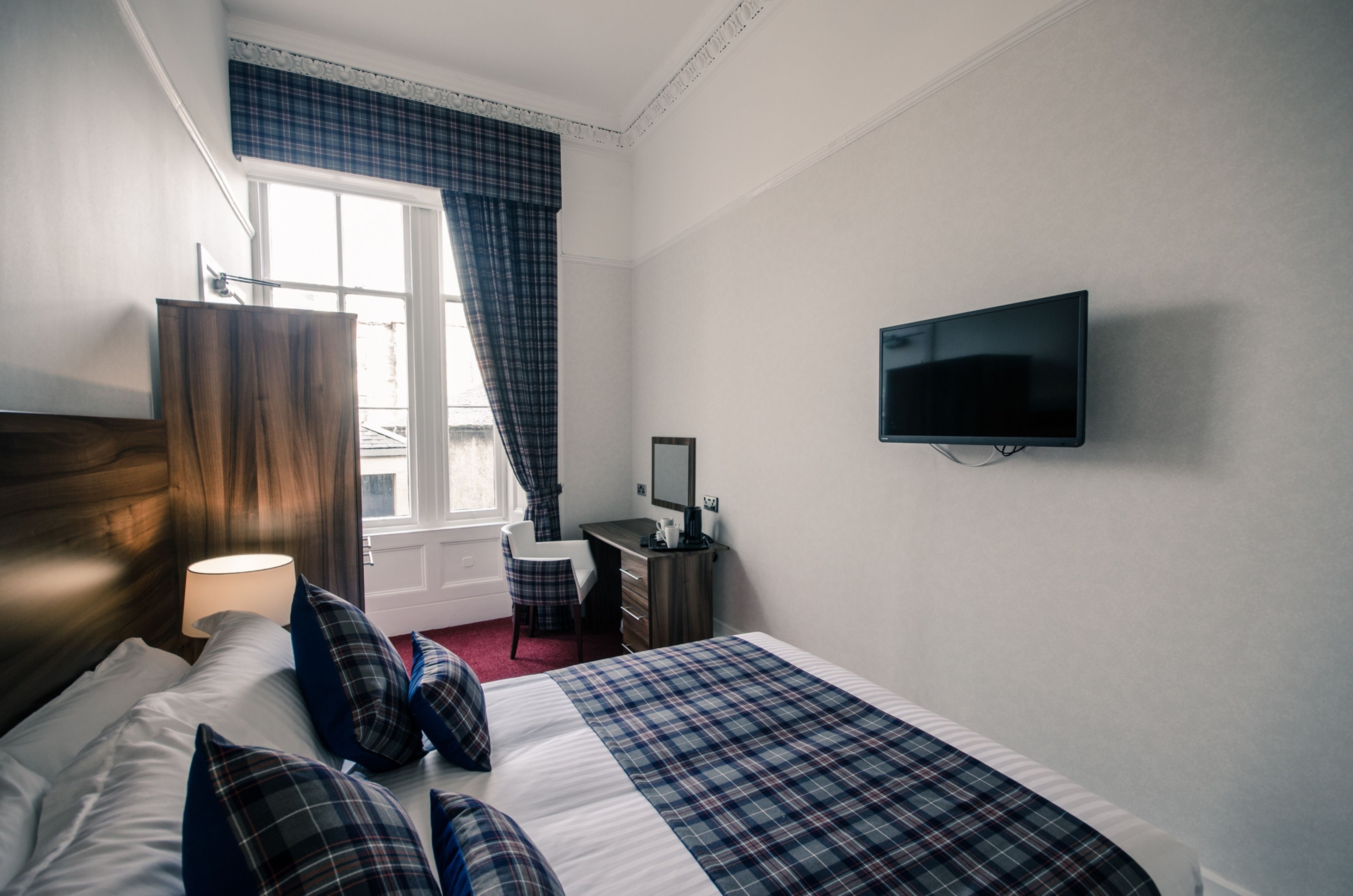 Ein Hotelzimmer mit Bett, Schreibtisch, Stuhl, Fernseher und einem Fenster mit Vorhängen.