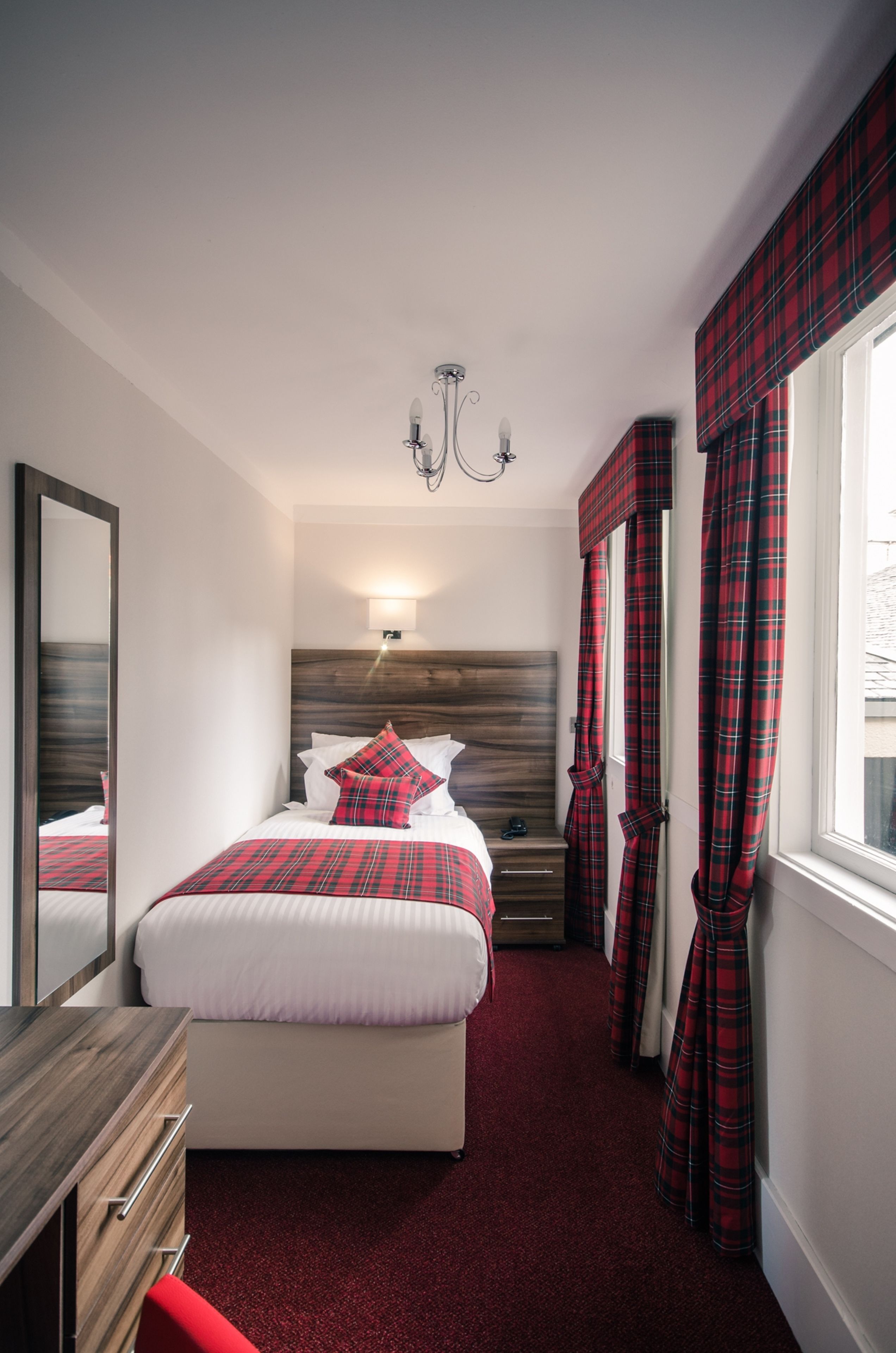 A bedroom with a bed, bedside table, lamp, and a mirror.