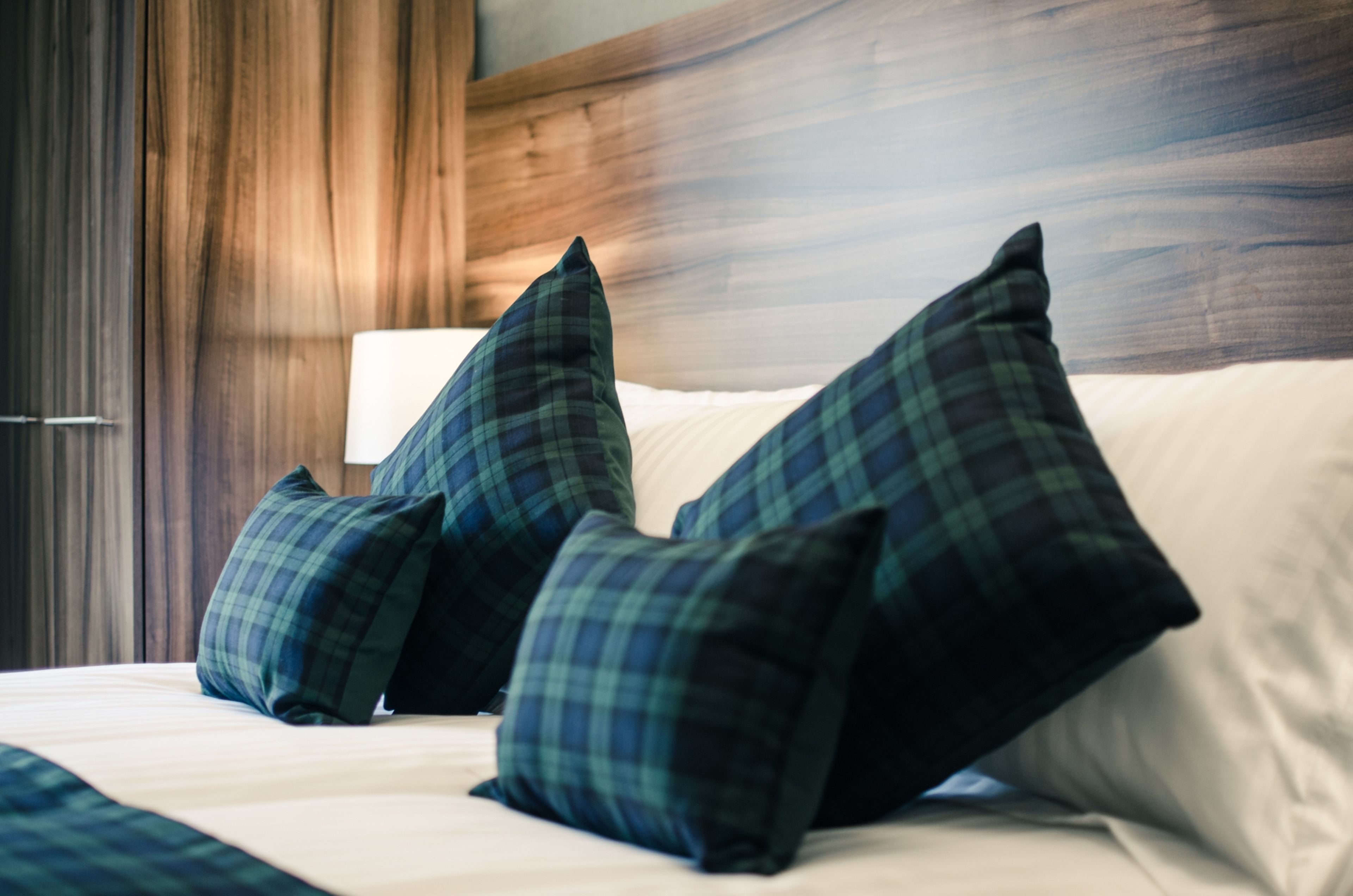 Cama com almofadas xadrez e cabeceira de madeira.