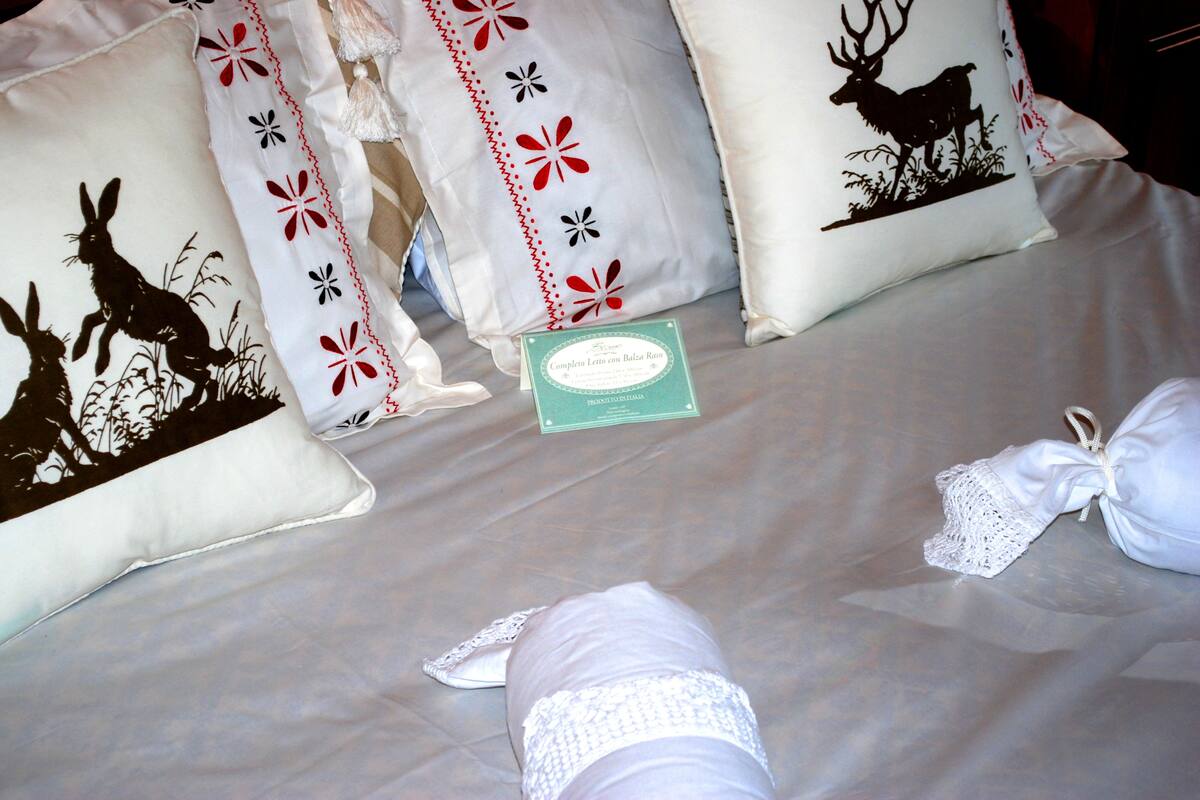 A neatly made bed with decorative pillows, a small card, and a folded white cloth.