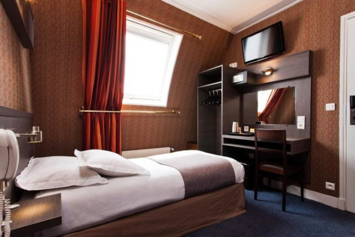 A hotel room with a bed, desk, chair, television, and a wardrobe.