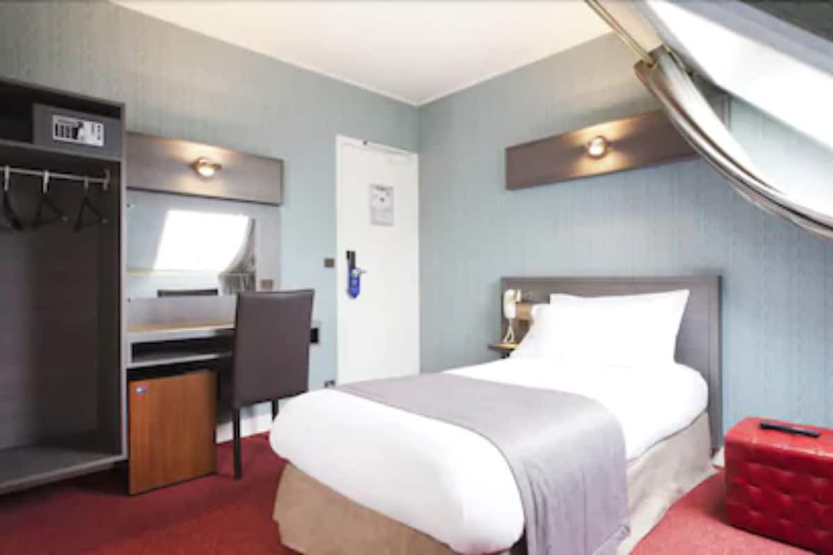 Quarto de hotel com cama, escrivaninha e guarda-roupa.
