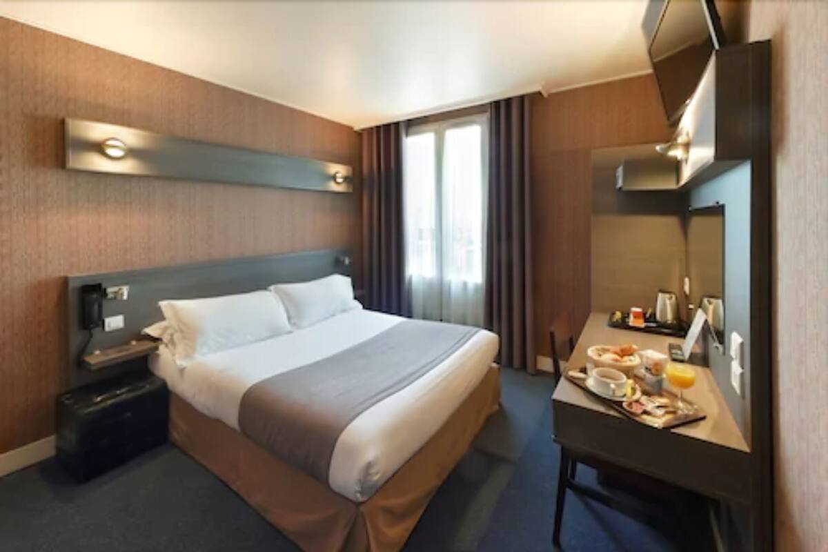 Quarto de hotel com uma cama grande, uma escrivaninha com itens de café da manhã, uma mala e um espelho.