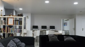 Ein modernes Wohnzimmer mit einer schwarzen Couch, einem Bücherregal und drei Computermonitoren auf einem Schreibtisch.