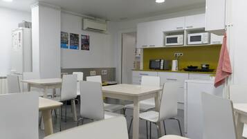 Una cocina moderna con armarios blancos, un microondas y un lavamanos. Hay sillas blancas alrededor de una mesa.