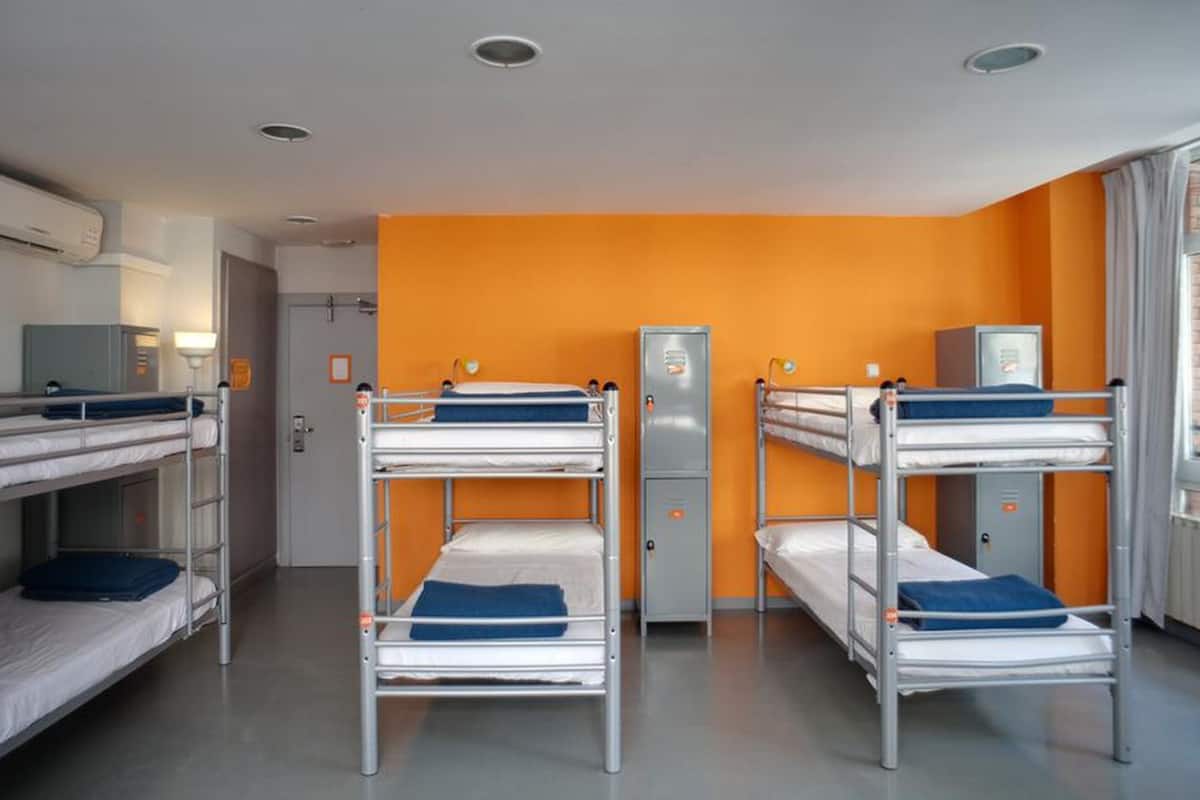Een slaapzaal met stapelbedden, een garderobe en een raam met gordijnen.