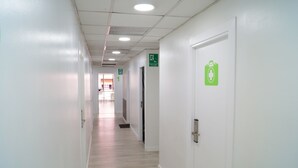 Ein sauberer, gut beleuchteter Flur mit weißen Wänden und Holzboden, der zu einer Tür führt, an der ein Notausgangsschild angebracht ist.