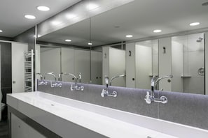 Ein modernes Badezimmer mit einem langen, weißen Waschbecken, mehreren Spiegeln und chromfarbenen Wasserhähnen.