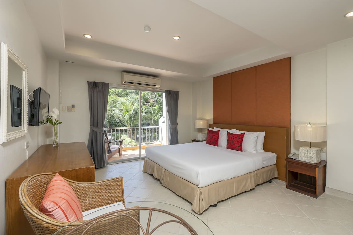 A hotel room with a large bed, a desk with a chair, a TV, and a balcony with curtains.