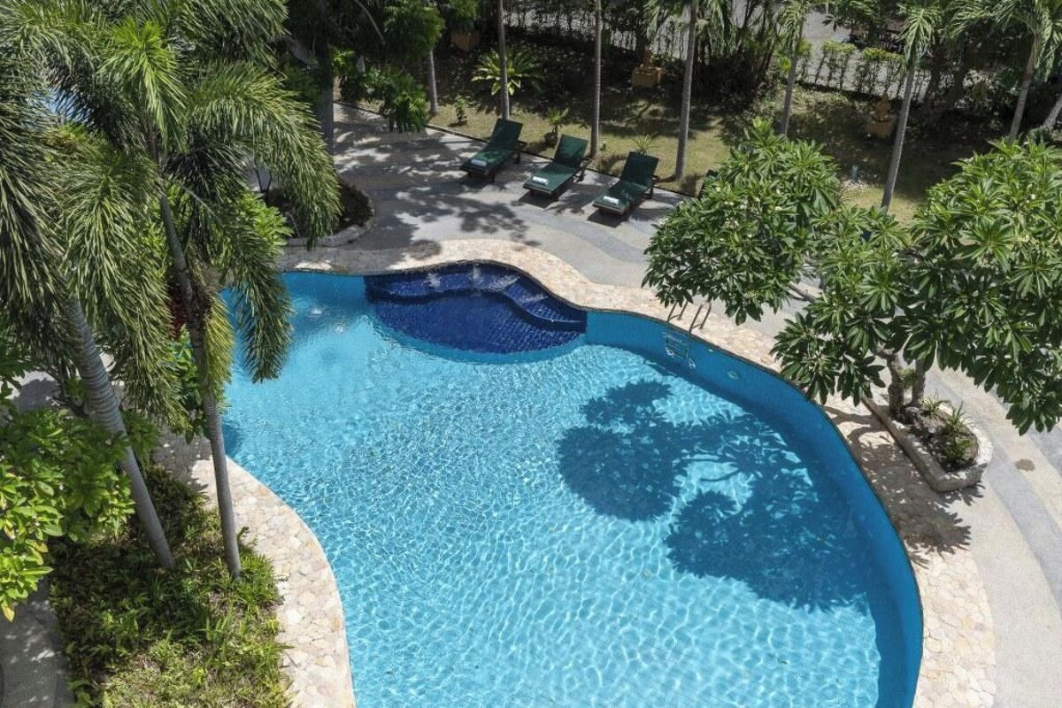 A swimming pool with a curved edge, surrounded by palm trees and lounge chairs.