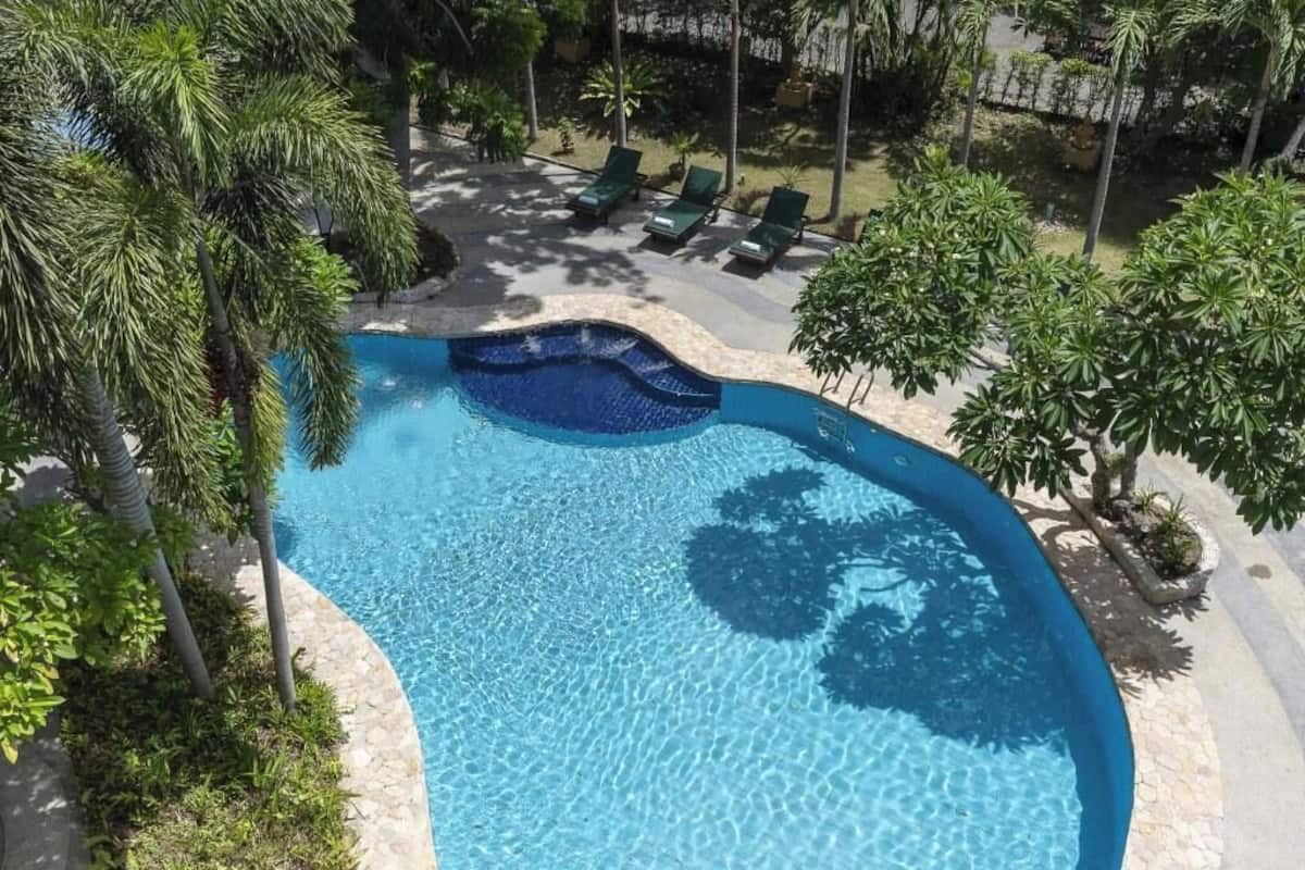 A swimming pool with a curved edge, surrounded by palm trees and lounge chairs.