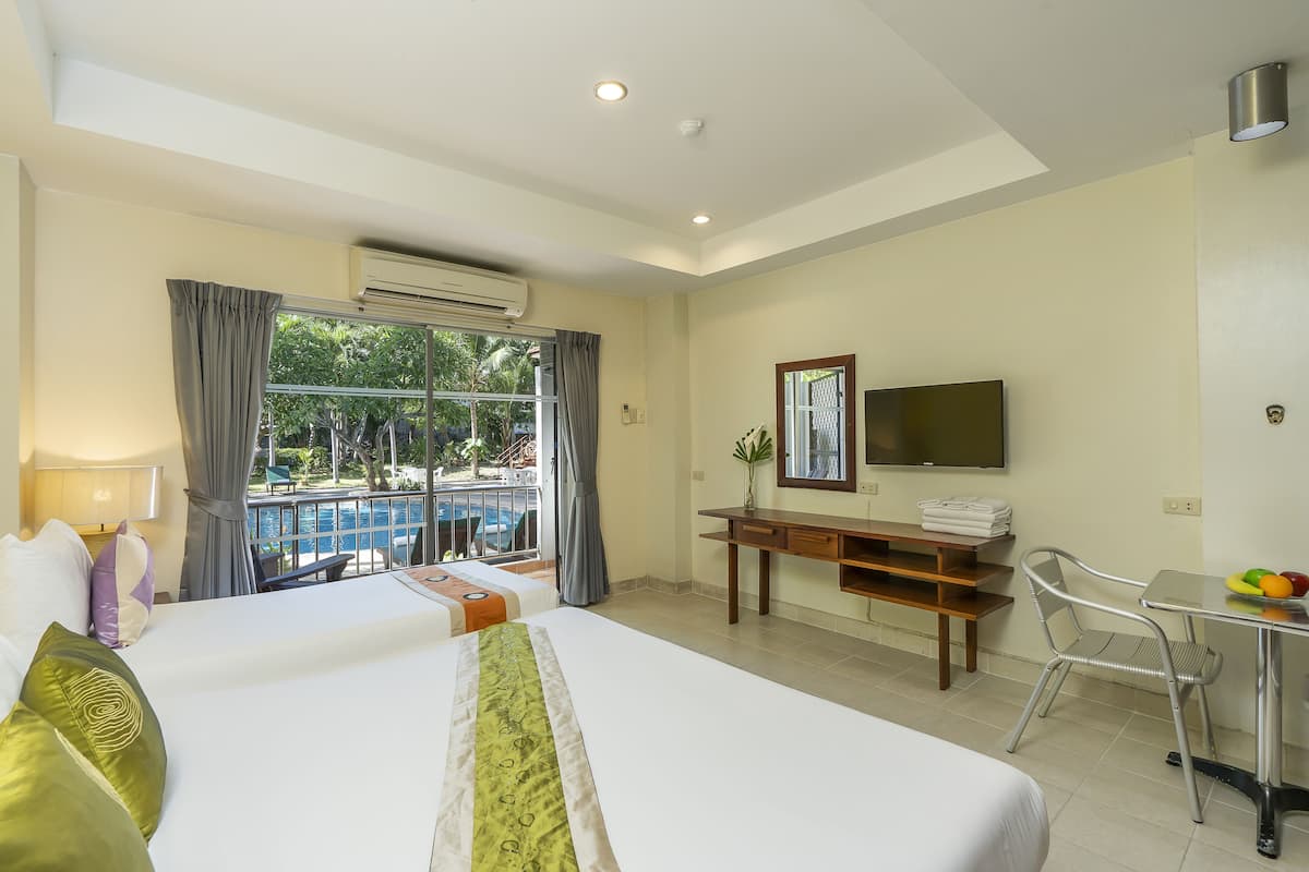A hotel room with two beds, a desk with a chair, a TV, and a view of a pool and greenery.
