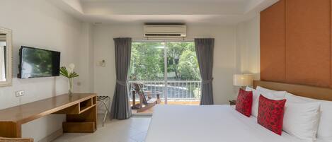 Een hotelkamer met een groot bed, een houten bureau, een televisie en een balkon met uitzicht op groen.