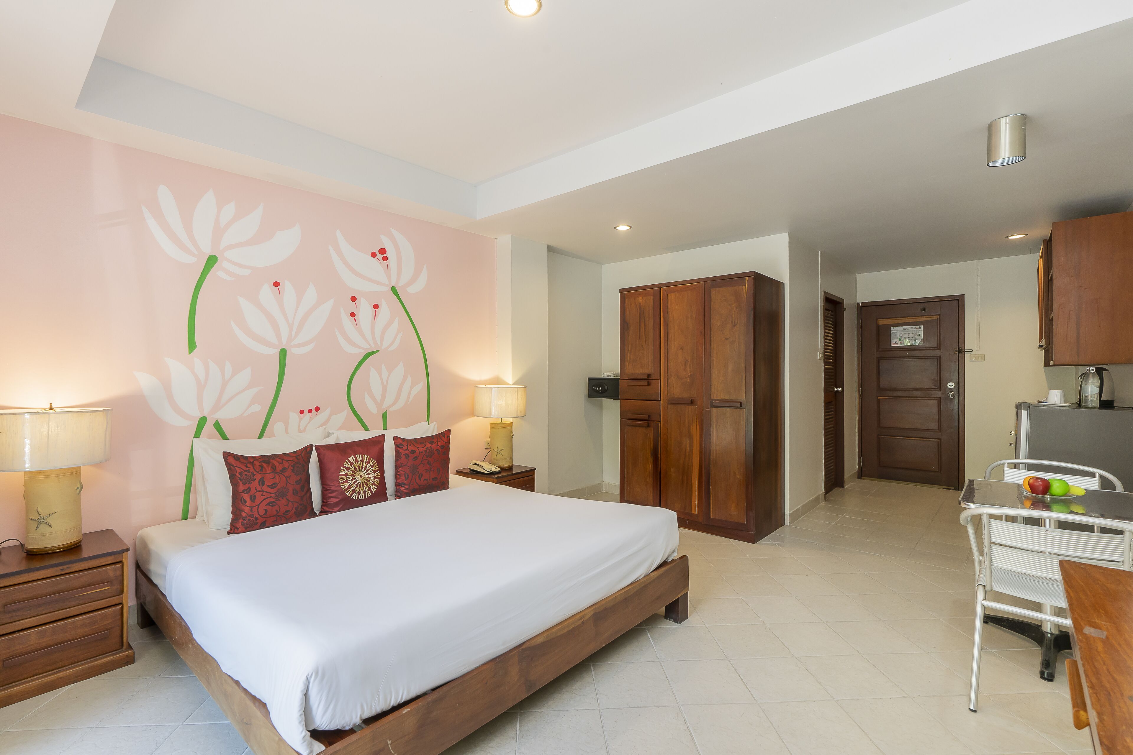 A bedroom with a bed, bedside tables, a desk, and a chair. There is a wooden wardrobe and a door leading to another room.