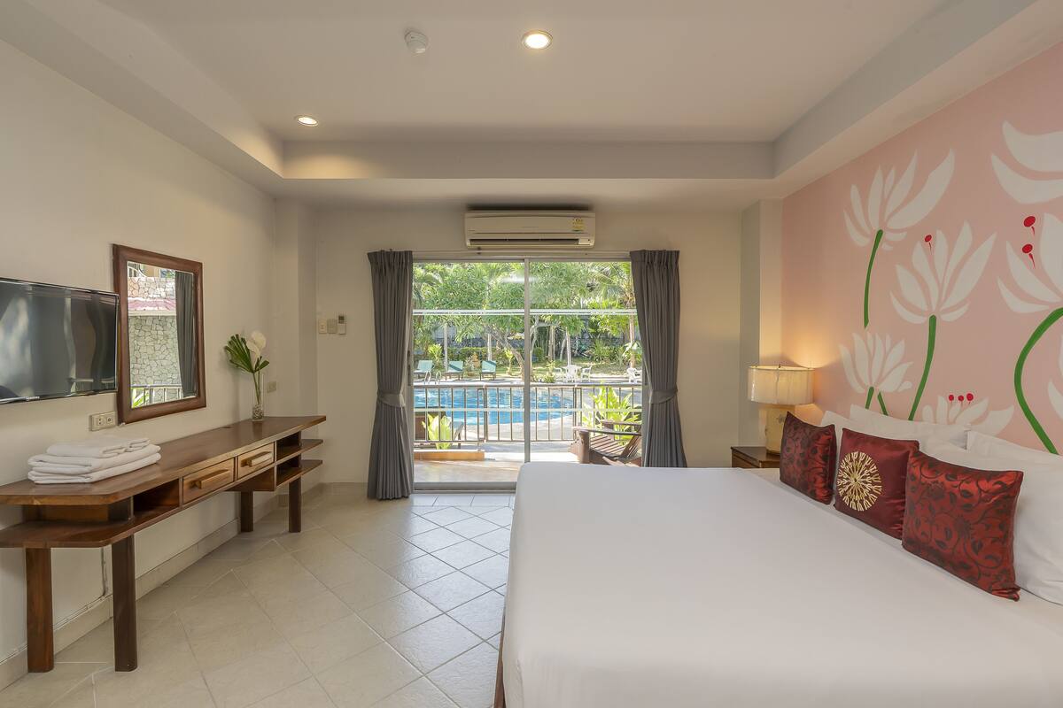 A hotel room with a bed, a desk, a TV, and a balcony with a pool view.