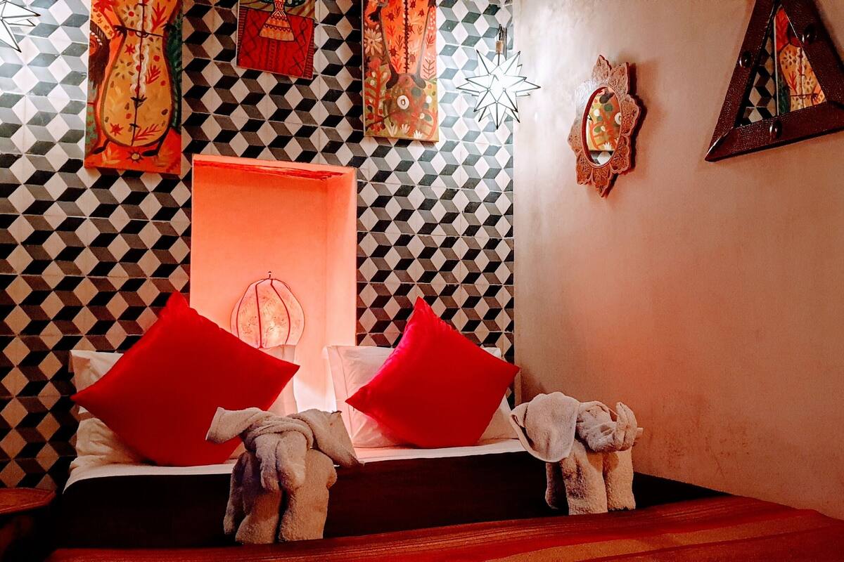 Una habitación de hotel con un estampado de cuadros en la pared, una cama con almohadas rojas y un ventanal con marco rojo.