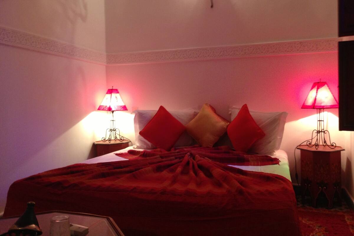 Una habitación de hotel con una cama bien hecha, dos lámparas de noche y un aplique decorativo.