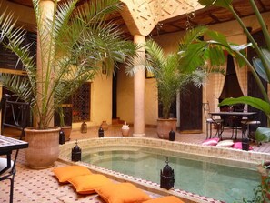A pool area with tiled flooring, potted plants, and a table with chairs.